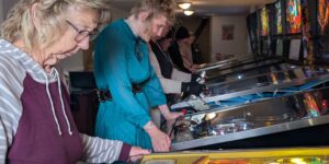 A group of women playing pinball machines at a tournament.