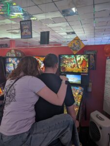 A person on their opponent's back while their opponent plays pinball. 